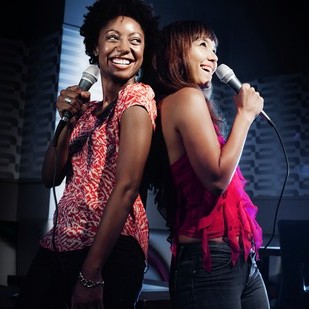 Two friends sing holding microphones.
